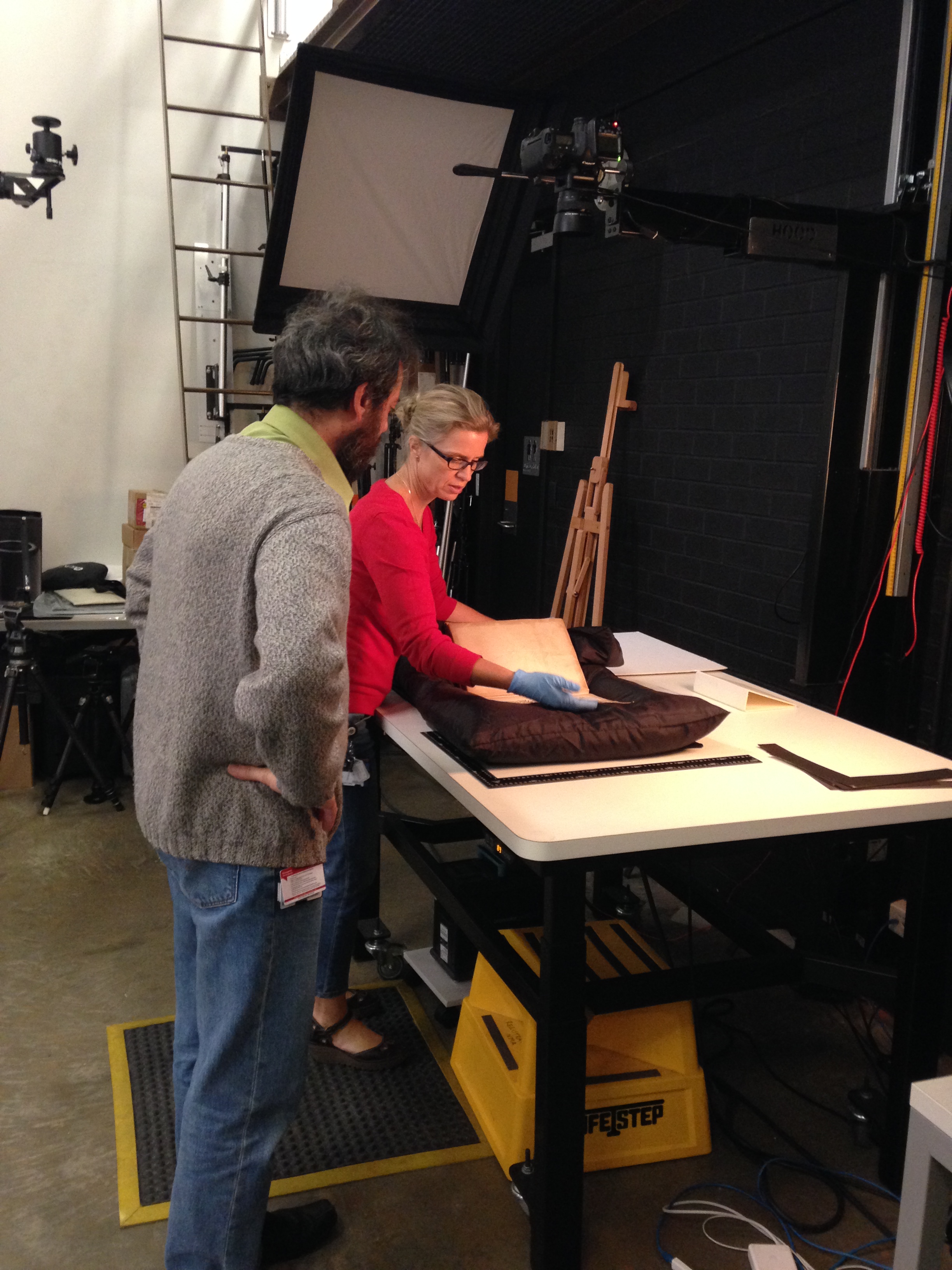 Senior conservator Tania Riviere and photographer George Serras discuss how to safely photograph the album. The object is cushioned on a 'pillow' to support the fragile spine as the pages are turned. Photograph by Kirsten Wehner.