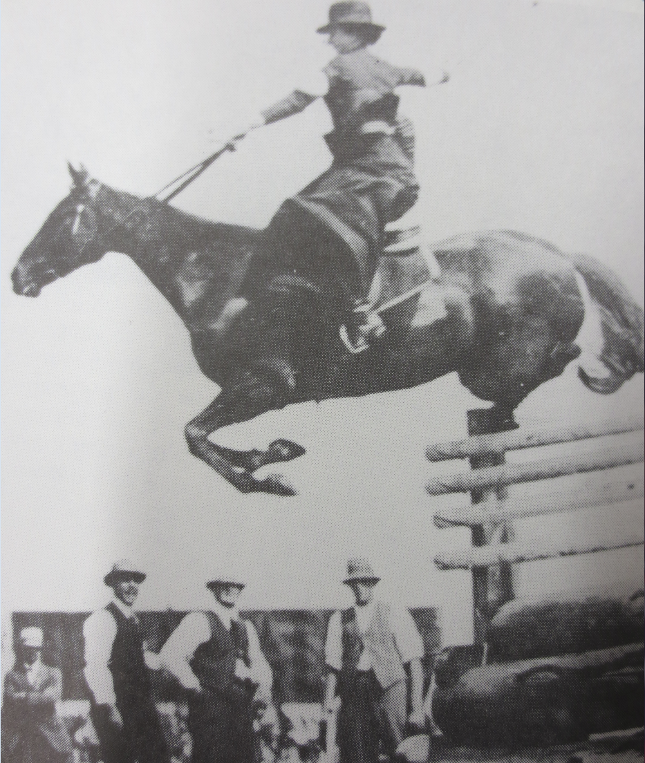 Woman jumping horse over jump using a sidesaddle