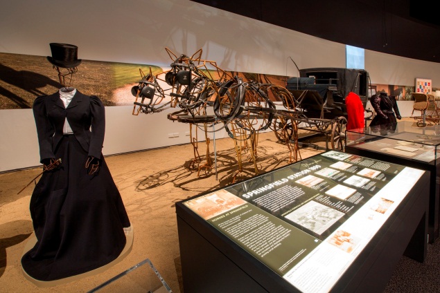 The Springfield exhibit in Spirited, featuring mannequins made by Harrie Fasher and Thylacine Exhibition Preparation. Left to right, riding habit worn by Constance Faithfull, paired harness and landau carriage, hunting pinks worn by William Anderson and dress worn by Florence Faithfull. Photograph by George Serras, National Museum of Australia.